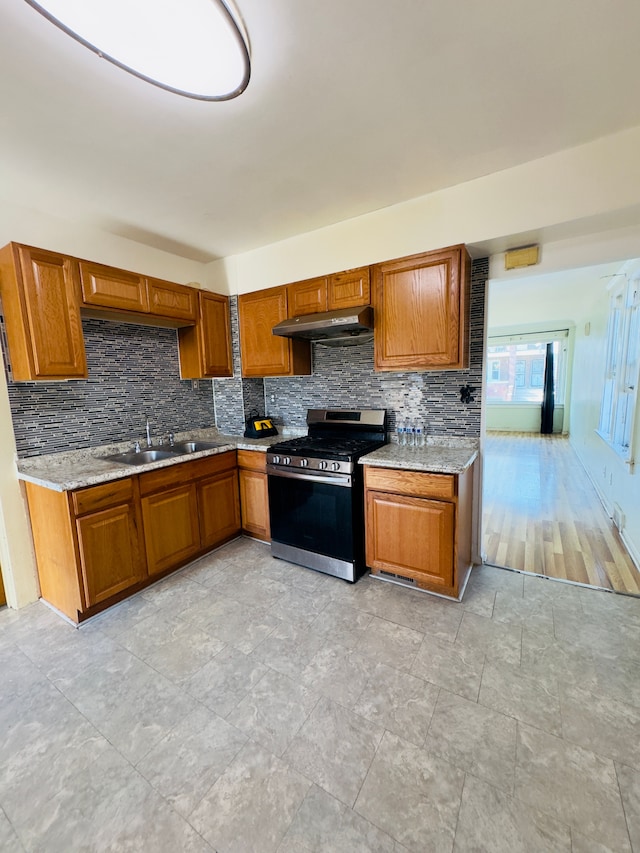 kitchen featuring brown cabinets, stainless steel gas stove, under cabinet range hood, and a sink