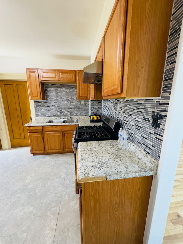 kitchen featuring tasteful backsplash, stainless steel range with gas cooktop, brown cabinets, exhaust hood, and a sink