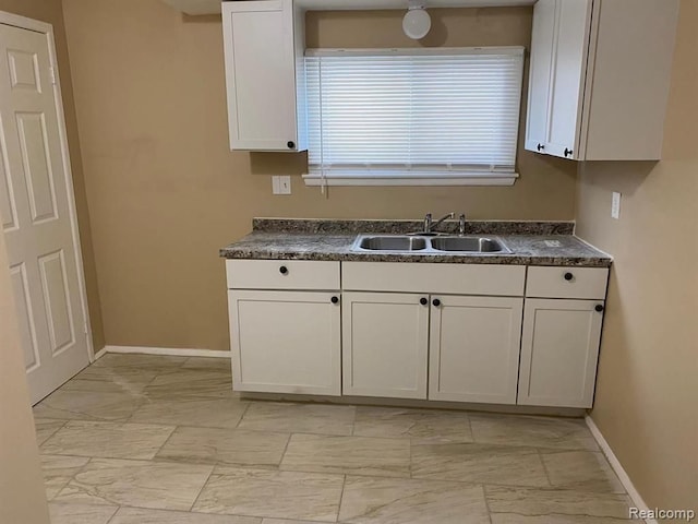 kitchen with dark countertops, a sink, baseboards, marble finish floor, and white cabinetry