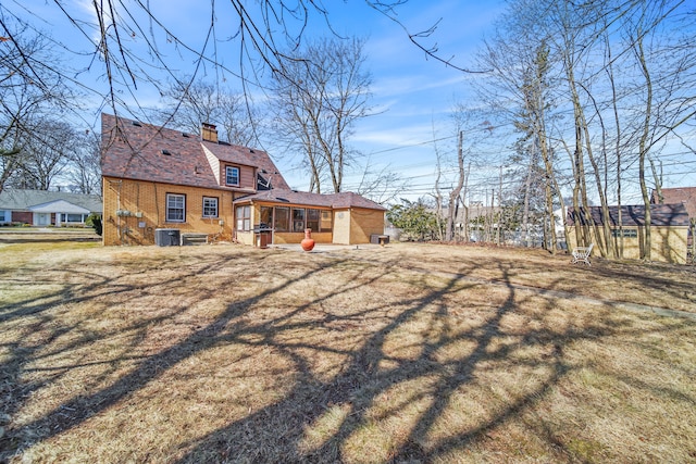 rear view of property featuring cooling unit, a lawn, brick siding, and a chimney