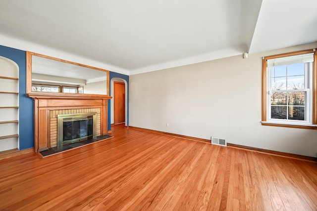 unfurnished living room featuring wood finished floors, visible vents, baseboards, arched walkways, and a brick fireplace