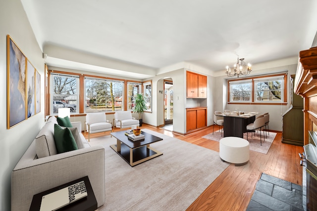 living room featuring arched walkways, a notable chandelier, light wood-type flooring, and a wealth of natural light