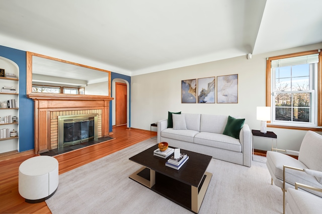 living area featuring arched walkways, a brick fireplace, baseboards, and wood finished floors