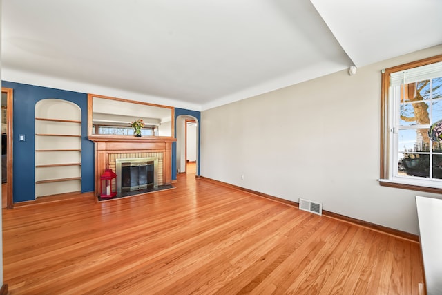 unfurnished living room featuring visible vents, built in shelves, a brick fireplace, baseboards, and wood finished floors