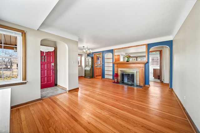 unfurnished living room featuring arched walkways, a chandelier, a brick fireplace, and light wood-style floors