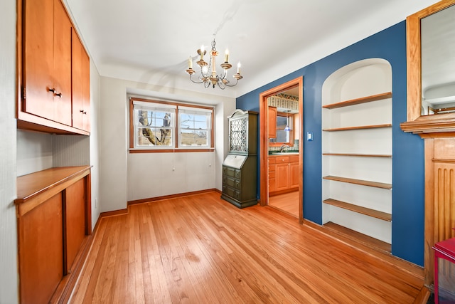 unfurnished dining area featuring a sink, light wood-type flooring, baseboards, and an inviting chandelier