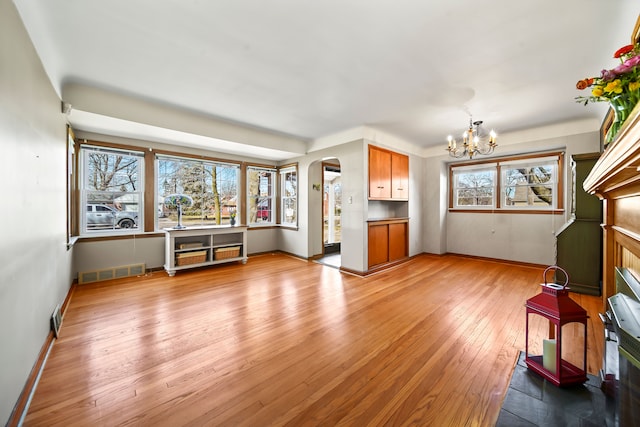 unfurnished living room featuring visible vents, baseboards, an inviting chandelier, arched walkways, and light wood-style floors