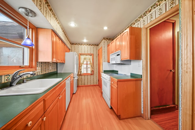 kitchen featuring a sink, white appliances, light wood-style floors, and wallpapered walls