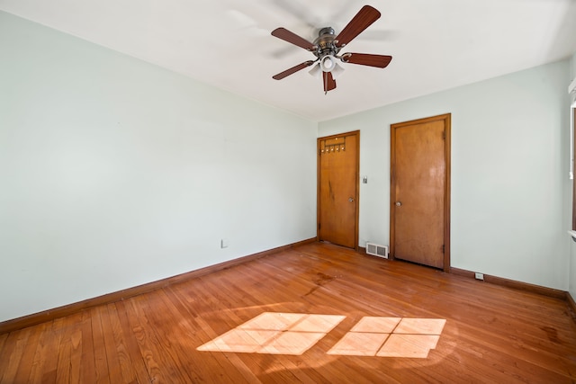 unfurnished bedroom featuring baseboards, visible vents, light wood-style flooring, ceiling fan, and two closets