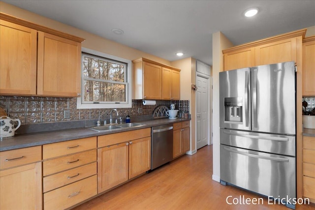 kitchen with dark countertops, tasteful backsplash, appliances with stainless steel finishes, light wood-style floors, and a sink