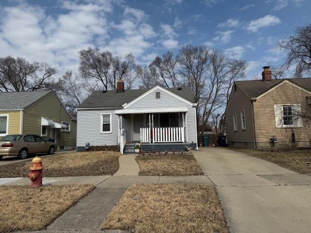 bungalow with concrete driveway, covered porch, and a chimney