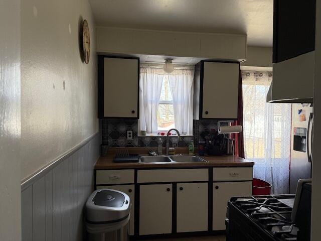 kitchen featuring tasteful backsplash, wainscoting, gas stove, white cabinetry, and a sink