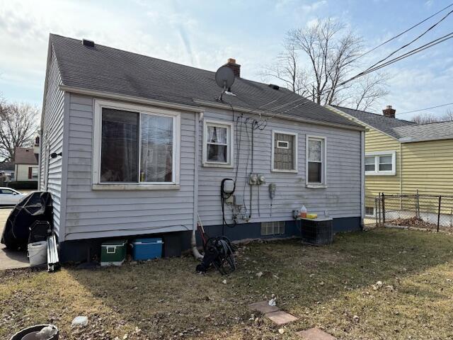 back of house featuring central AC unit, fence, a yard, a shingled roof, and a chimney