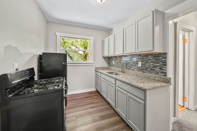 kitchen featuring baseboards, a sink, black range with gas stovetop, light wood-type flooring, and backsplash