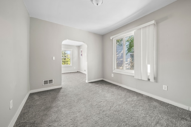 carpeted empty room featuring arched walkways, visible vents, and baseboards