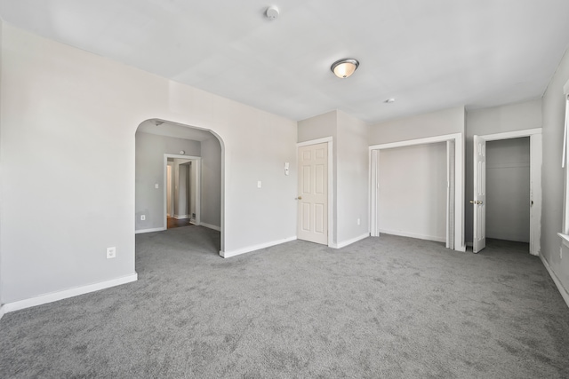 unfurnished bedroom with arched walkways, baseboards, and carpet floors