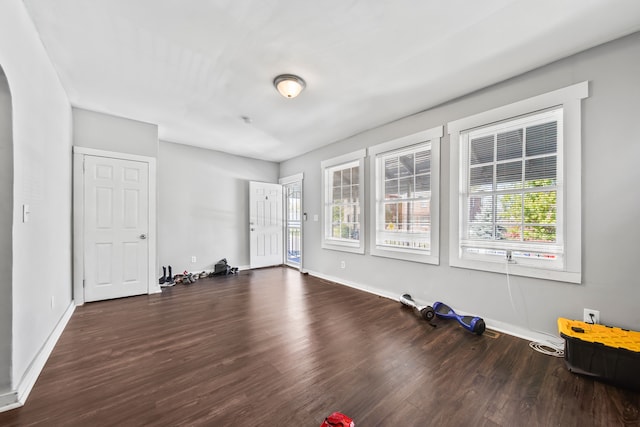 unfurnished room featuring dark wood-style floors, baseboards, and arched walkways