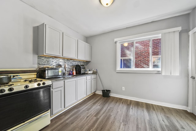 kitchen featuring dark wood-type flooring, stainless steel microwave, backsplash, range with gas cooktop, and baseboards