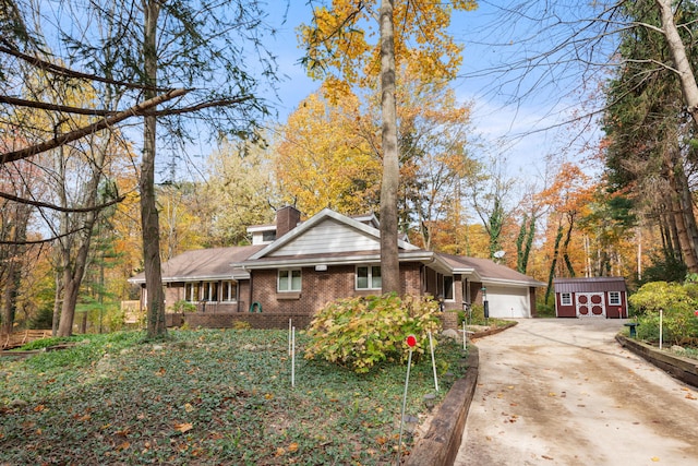 view of front of house with driveway, a shed, a garage, brick siding, and a chimney