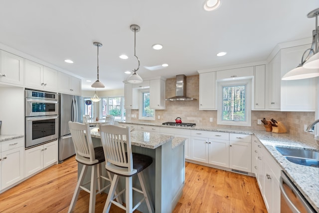 kitchen with light wood finished floors, stainless steel appliances, a sink, white cabinets, and wall chimney exhaust hood