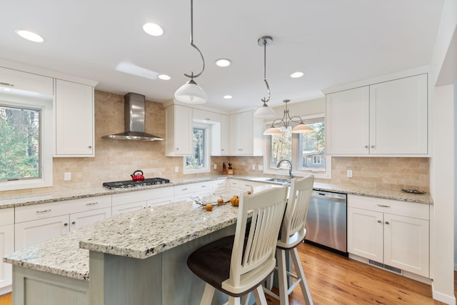 kitchen with light wood-style flooring, appliances with stainless steel finishes, white cabinets, and wall chimney range hood