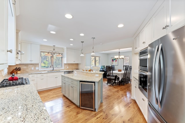 kitchen with tasteful backsplash, beverage cooler, light wood-style flooring, appliances with stainless steel finishes, and an inviting chandelier