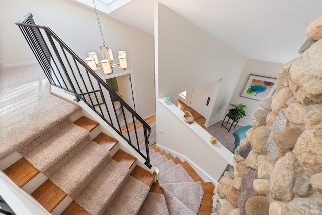 stairs with baseboards, lofted ceiling with skylight, and a chandelier