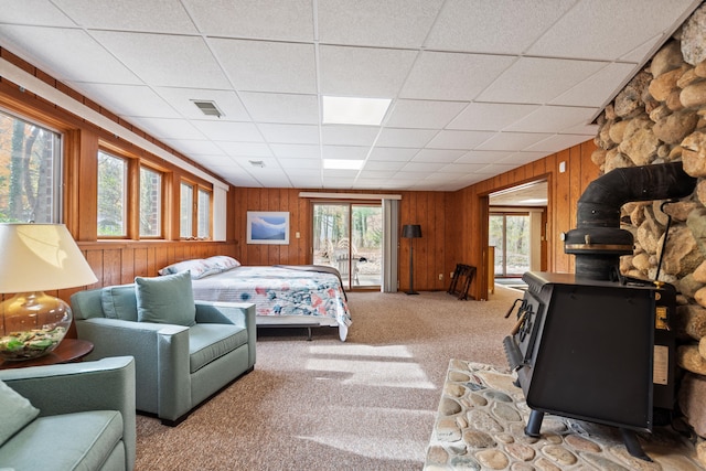 carpeted bedroom with visible vents, wood walls, a wood stove, and a drop ceiling