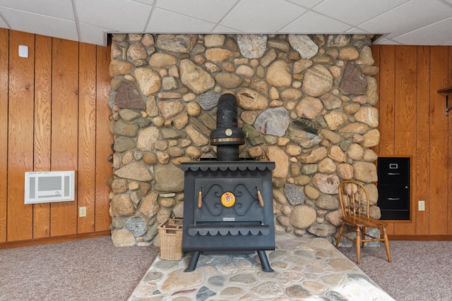 interior details featuring a wood stove, a paneled ceiling, wooden walls, and carpet flooring