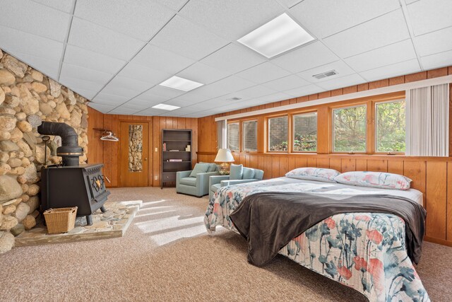 carpeted bedroom featuring a wood stove, a drop ceiling, visible vents, and wood walls