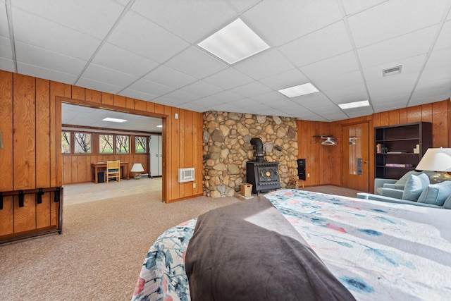 carpeted bedroom with a wood stove, wooden walls, a paneled ceiling, and visible vents