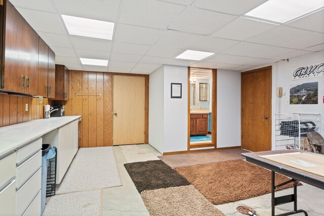 kitchen with a drop ceiling, baseboards, wood walls, and light countertops