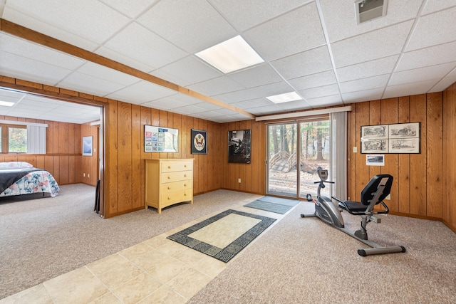 workout area with wooden walls, light colored carpet, visible vents, and a drop ceiling