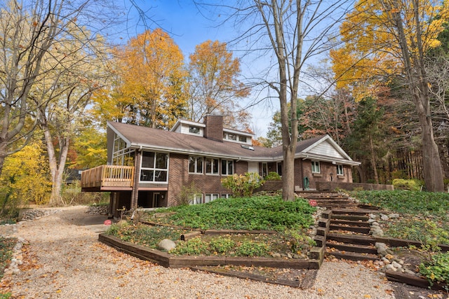 view of front facade featuring driveway, a vegetable garden, a sunroom, a chimney, and brick siding