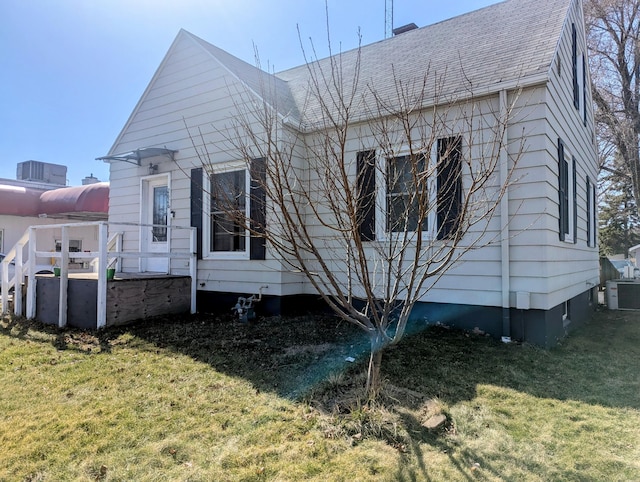 rear view of house with central air condition unit, a lawn, and roof with shingles