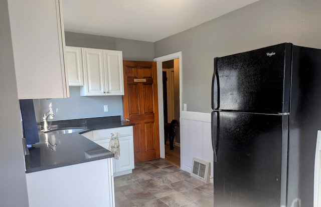 kitchen featuring dark countertops, visible vents, freestanding refrigerator, white cabinets, and a sink