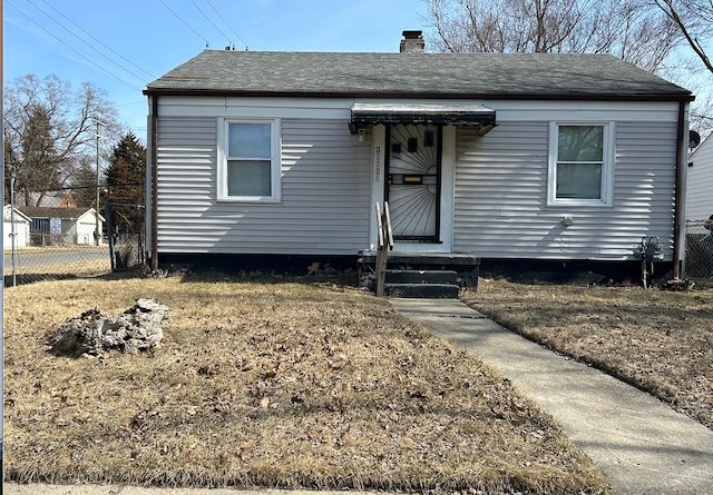 bungalow featuring fence, roof with shingles, and a chimney