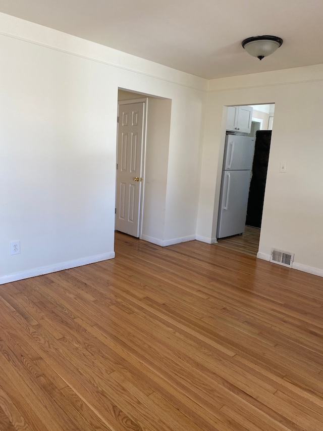 empty room with visible vents, light wood-type flooring, and baseboards