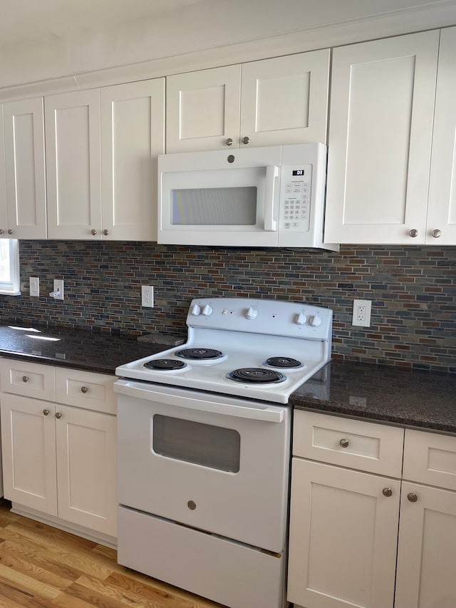 kitchen with light wood-style flooring, dark stone countertops, tasteful backsplash, white cabinetry, and white appliances