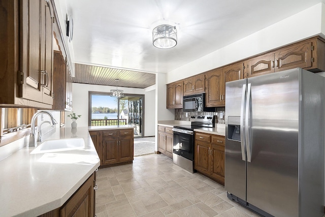 kitchen with a notable chandelier, a sink, appliances with stainless steel finishes, light countertops, and decorative backsplash