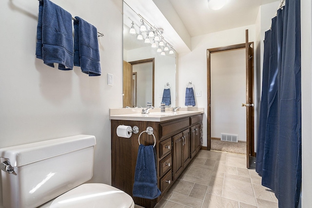 bathroom with visible vents, toilet, a sink, double vanity, and baseboards