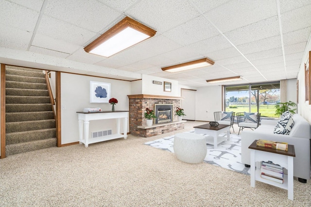 living room with visible vents, a brick fireplace, a drop ceiling, stairway, and carpet floors