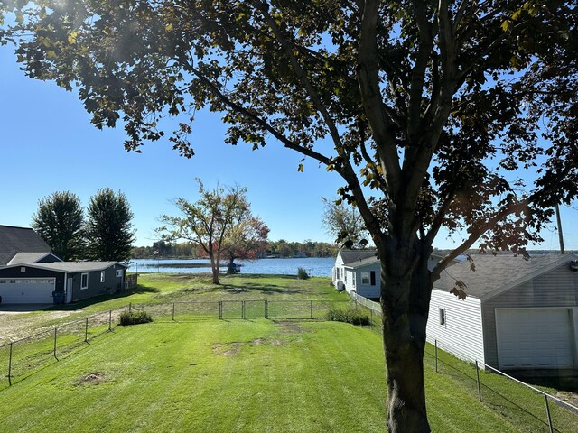 view of yard with a water view, driveway, an attached garage, and fence