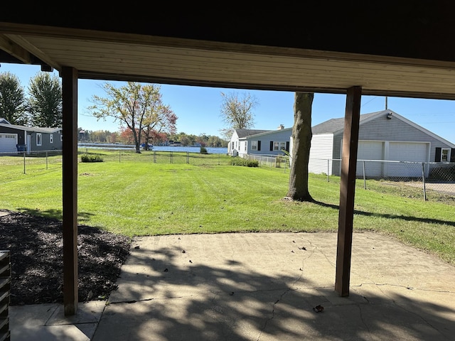 view of yard with a patio area, a garage, fence, and a water view