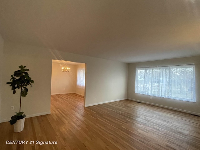 unfurnished room featuring a notable chandelier, wood finished floors, and baseboards