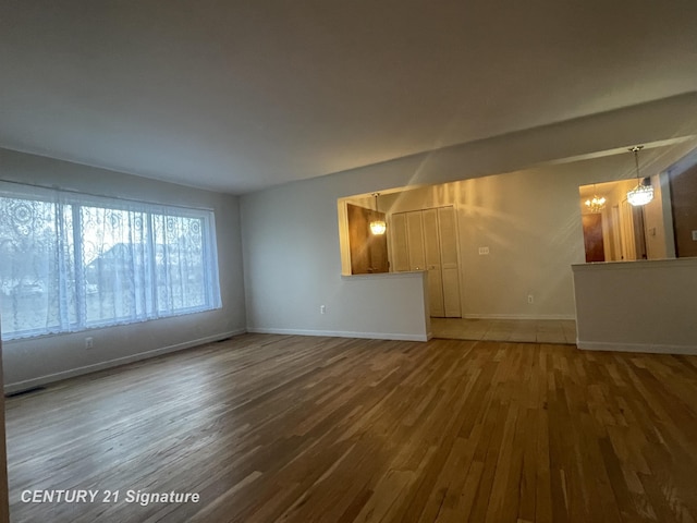 unfurnished living room with wood finished floors, baseboards, and a chandelier