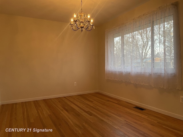 spare room with visible vents, baseboards, an inviting chandelier, and wood finished floors