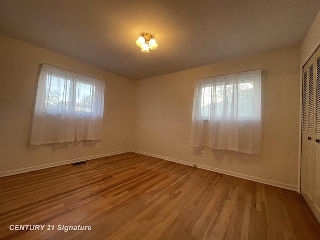 unfurnished bedroom featuring visible vents, baseboards, a closet, and wood finished floors