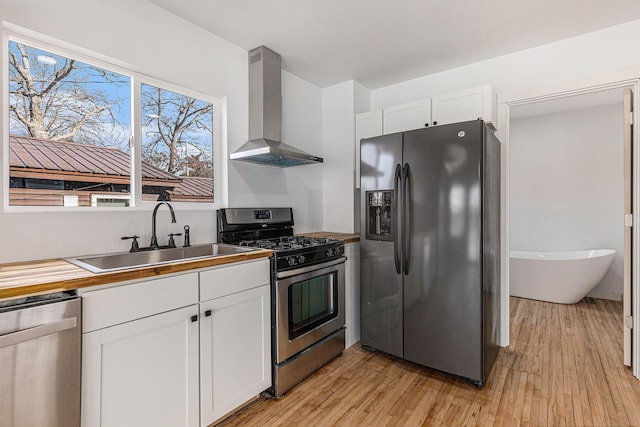 5557 Front St, Newaygo, MI 49337 - kitchen with light wood finished floors, a sink, appliances with stainless steel finishes, white cabinetry, and wall chimney range hood