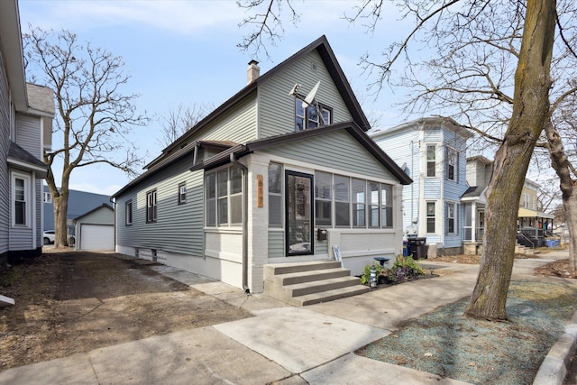 view of front of home with a detached garage, a chimney, an outdoor structure, a sunroom, and driveway